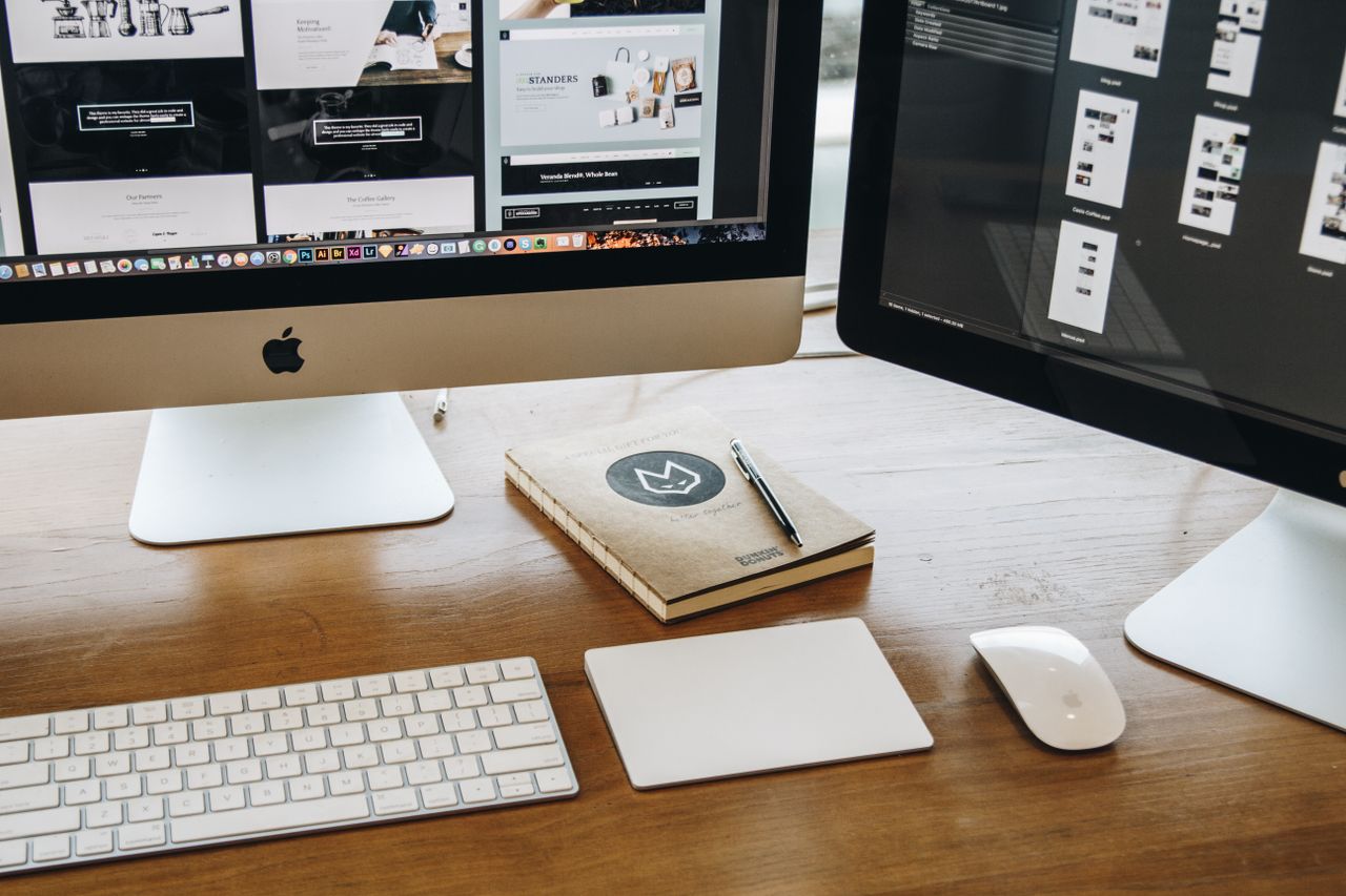 A clean, minimalist desk arrangement with dual monitors, a keyboard, mouse, and notebook designed to support productivity.